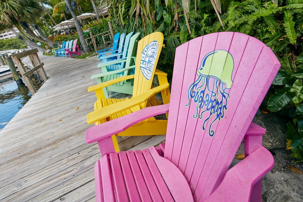 A hot-pink Adirondack chair with the Guanabanas jellyfish logo on the back, a row of bright chairs receding down the boardwalk